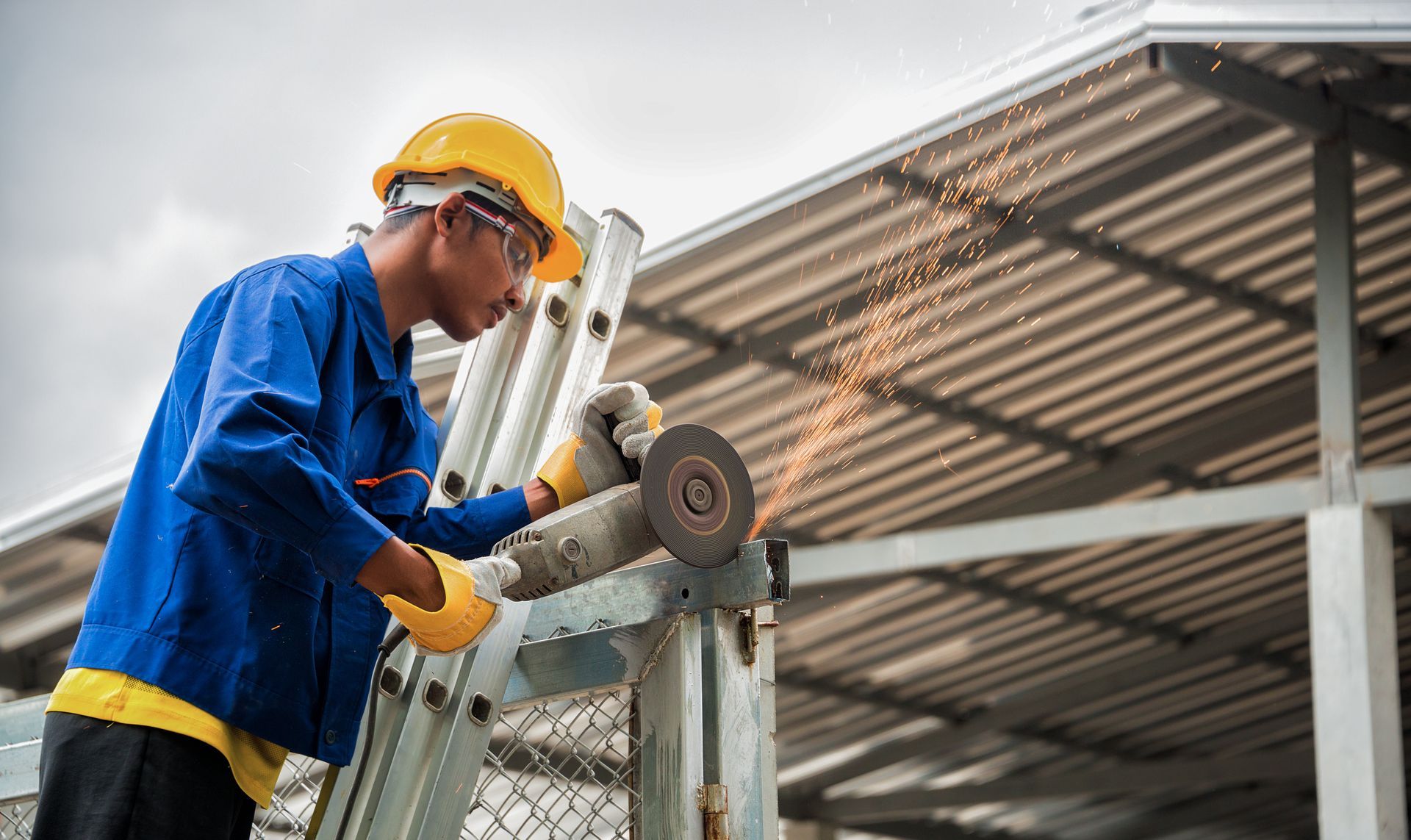 Construction worker in yellow helmet and safety glasses using a grinder outdoors, sparks flying.