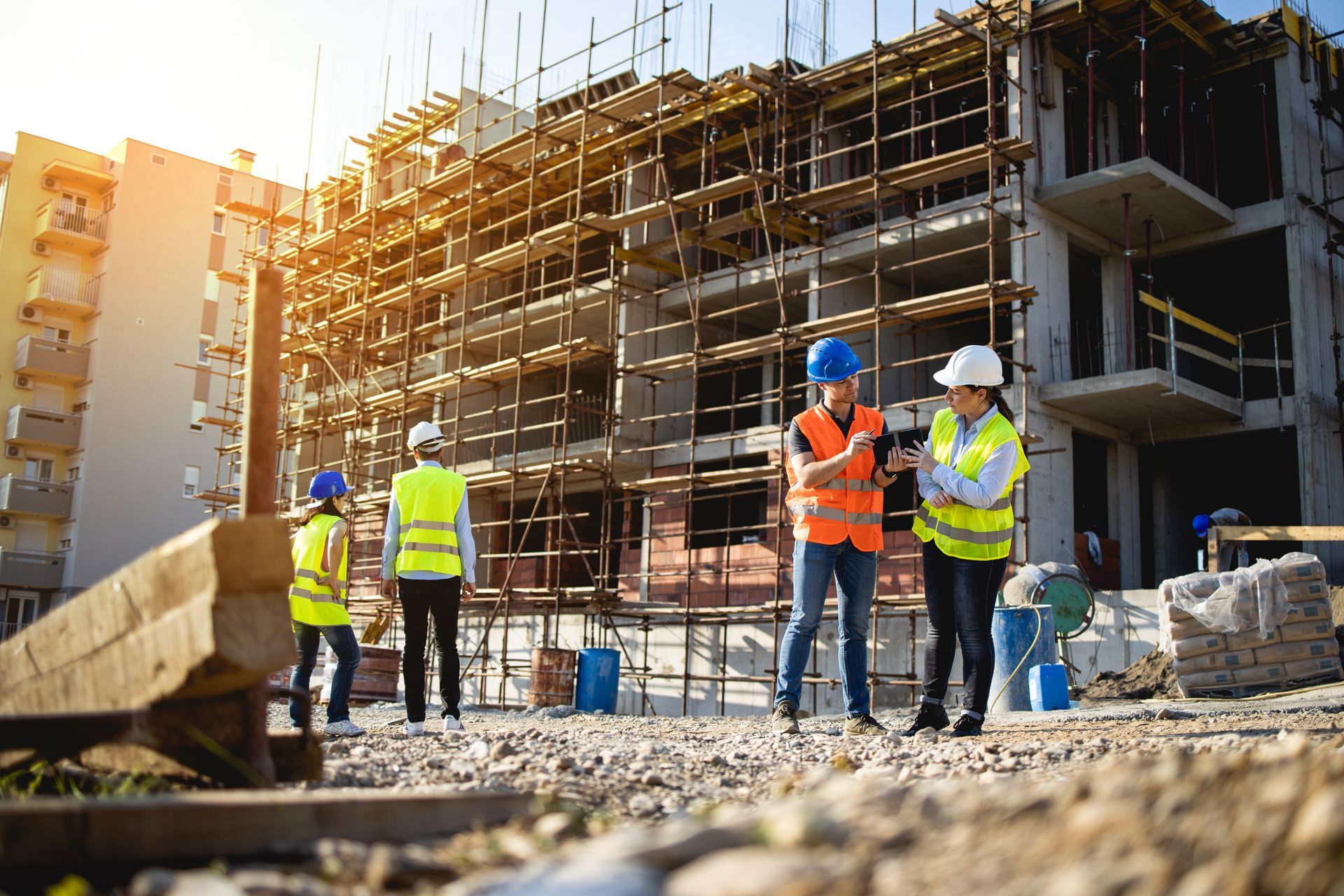 Construction workers at a building site, wearing safety vests and helmets. Sunlit setting.