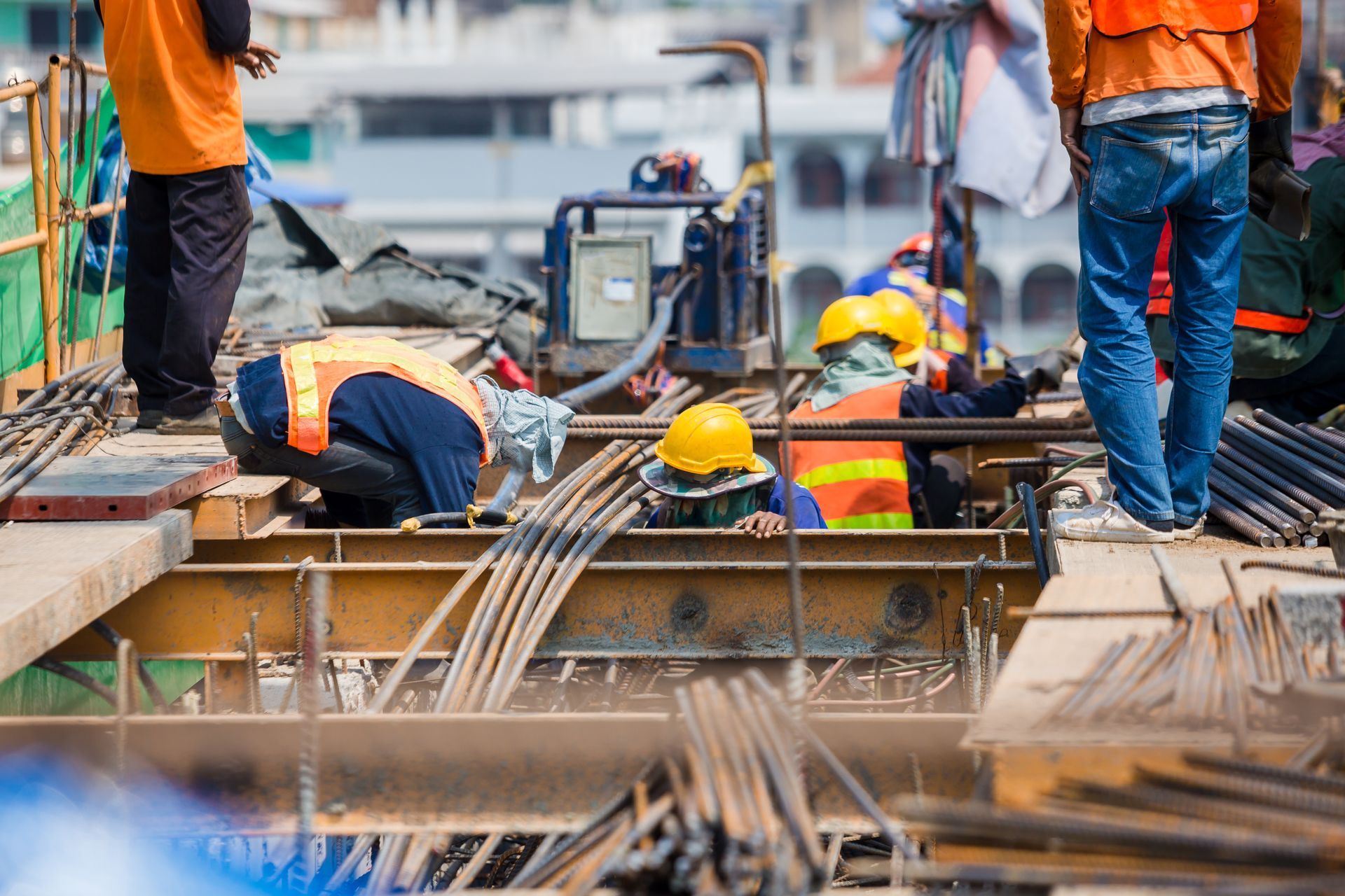 Construction workers in orange vests and hard hats working on rebar at a construction site.
