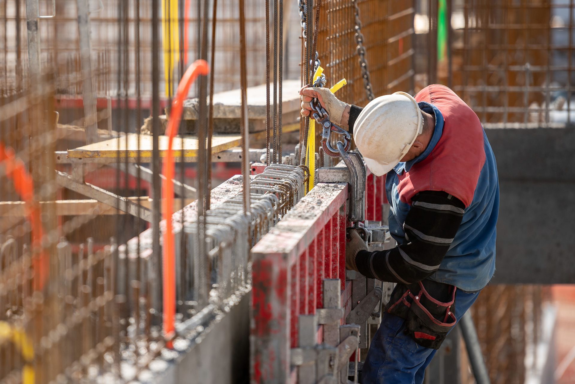 Construction worker in hard hat attaching equipment to concrete formwork.