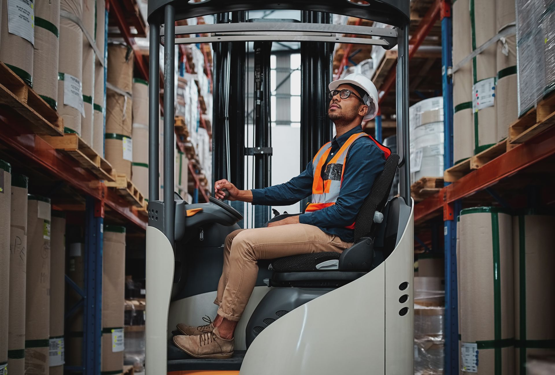 Person in safety gear operating a forklift inside a warehouse, looking upward.