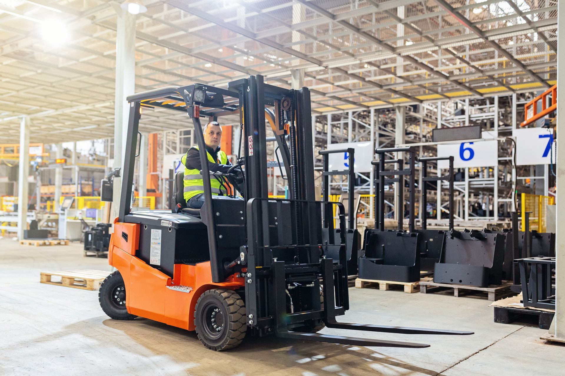 Forklift in orange and black, driven by person in a yellow safety vest inside a warehouse.