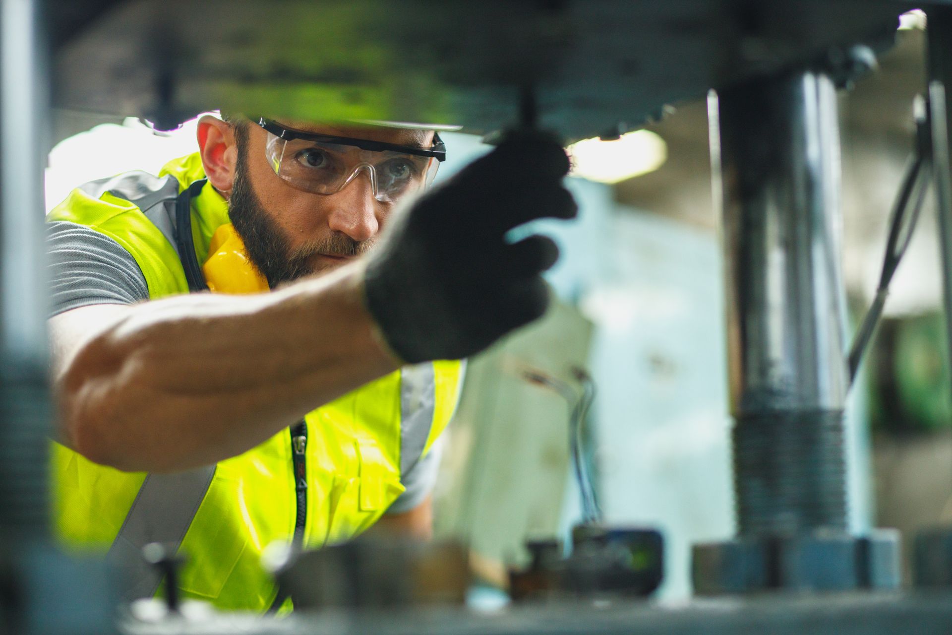 Man in safety vest and goggles working on machinery.