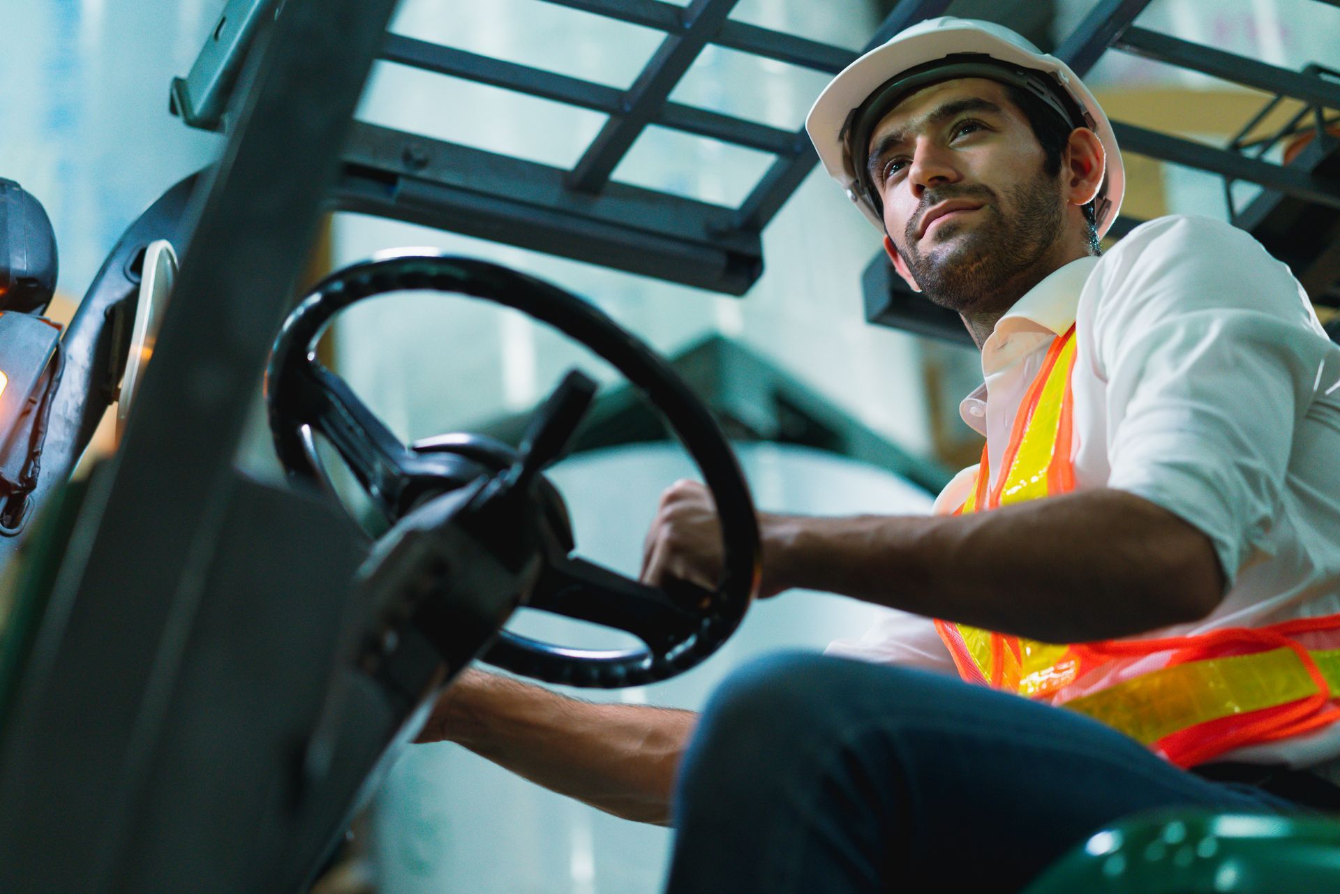 Man in hard hat and safety vest driving a forklift in a warehouse.