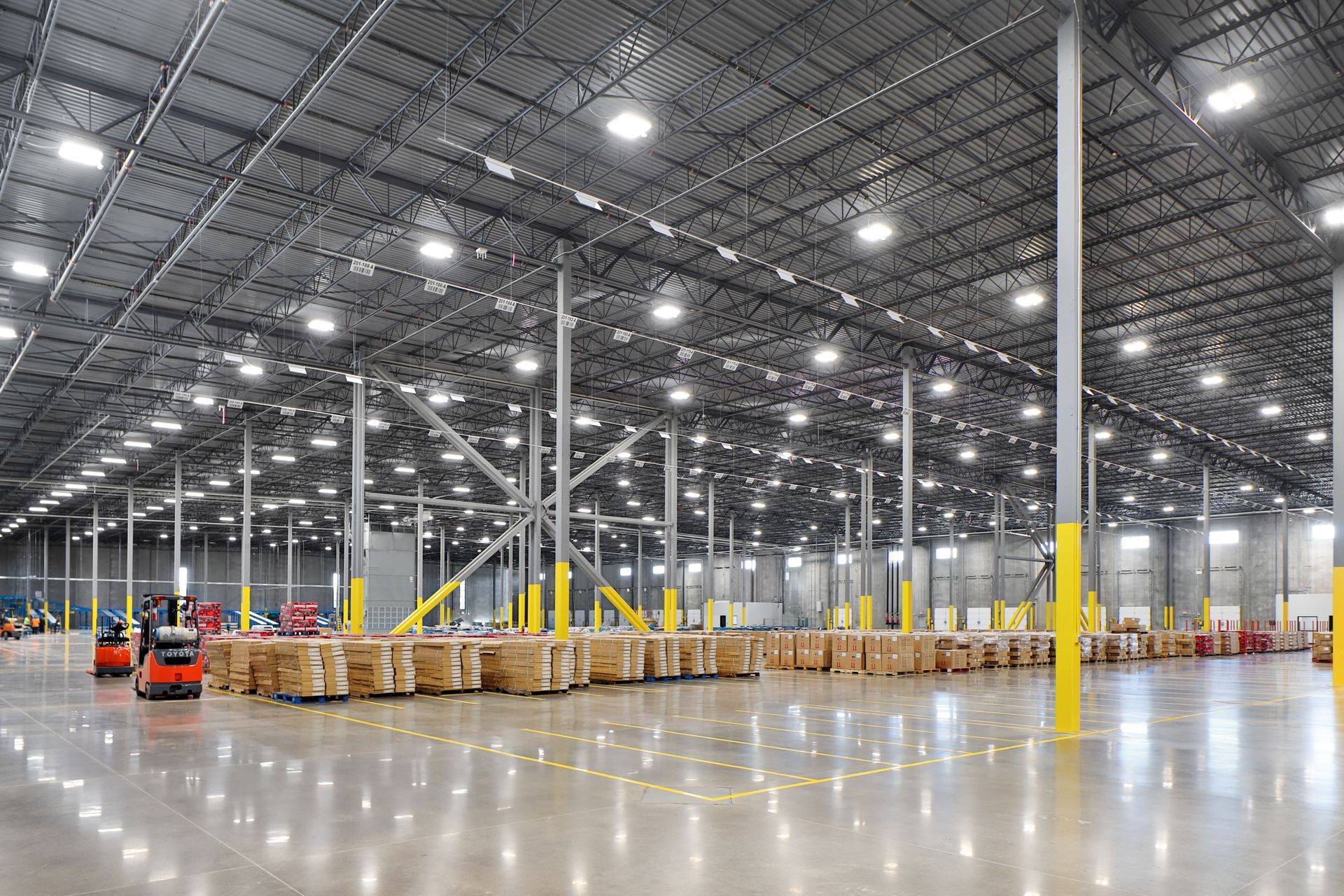 Large, open warehouse with pallets of goods, forklifts, and overhead lighting.