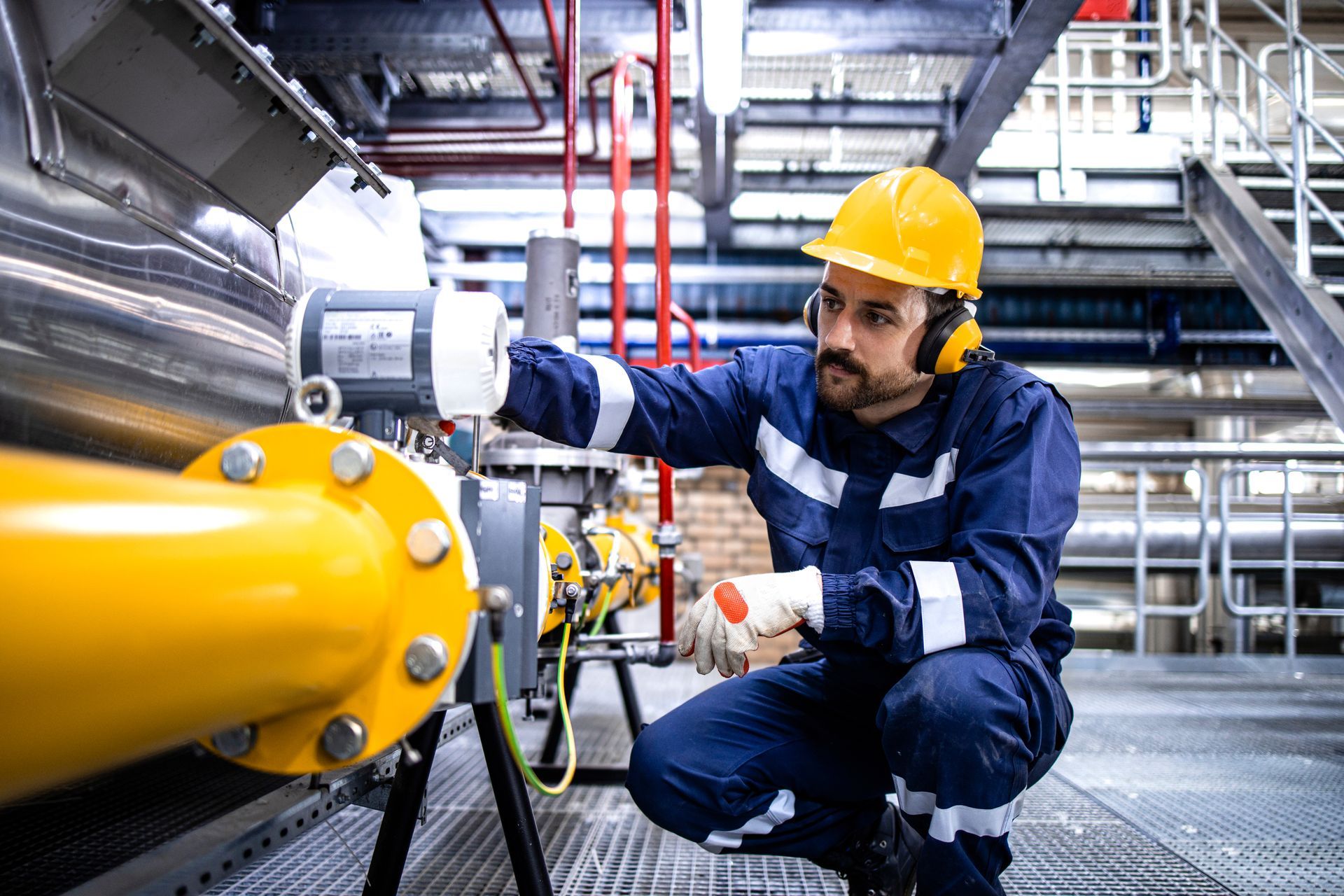 Worker in yellow hard hat inspecting machinery in industrial setting. Worker in yellow hard hat inspecting machinery in industrial setting.