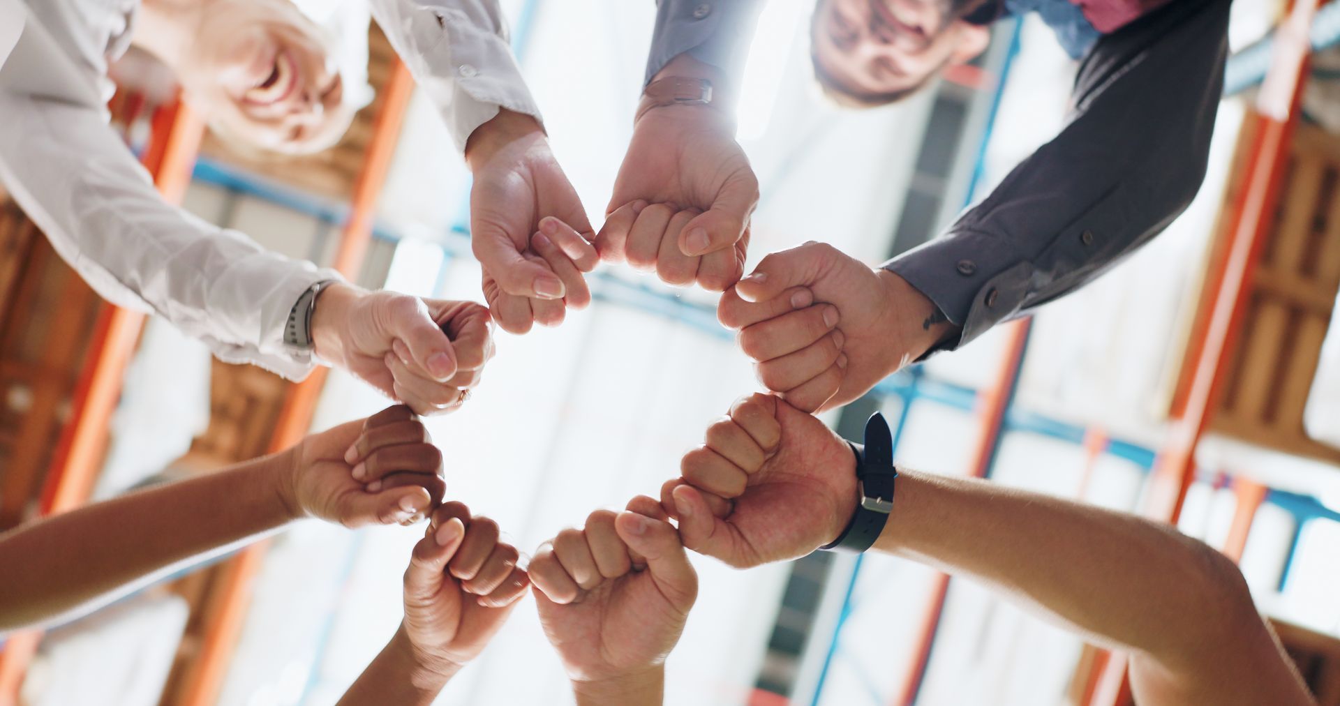 People joining fists in a circle, viewed from below. Warehouse setting.