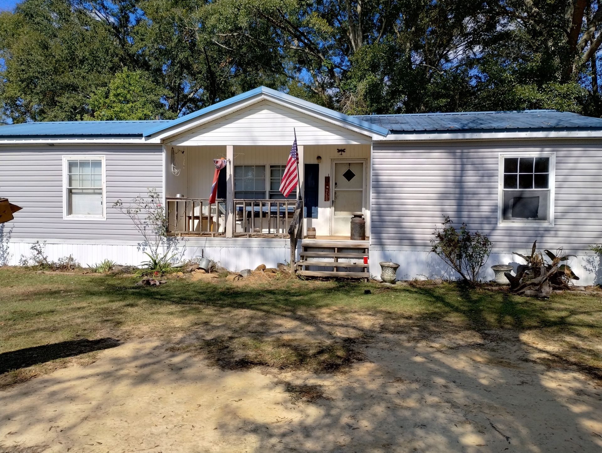 A mobile home with a blue roof and an american flag on the porch.