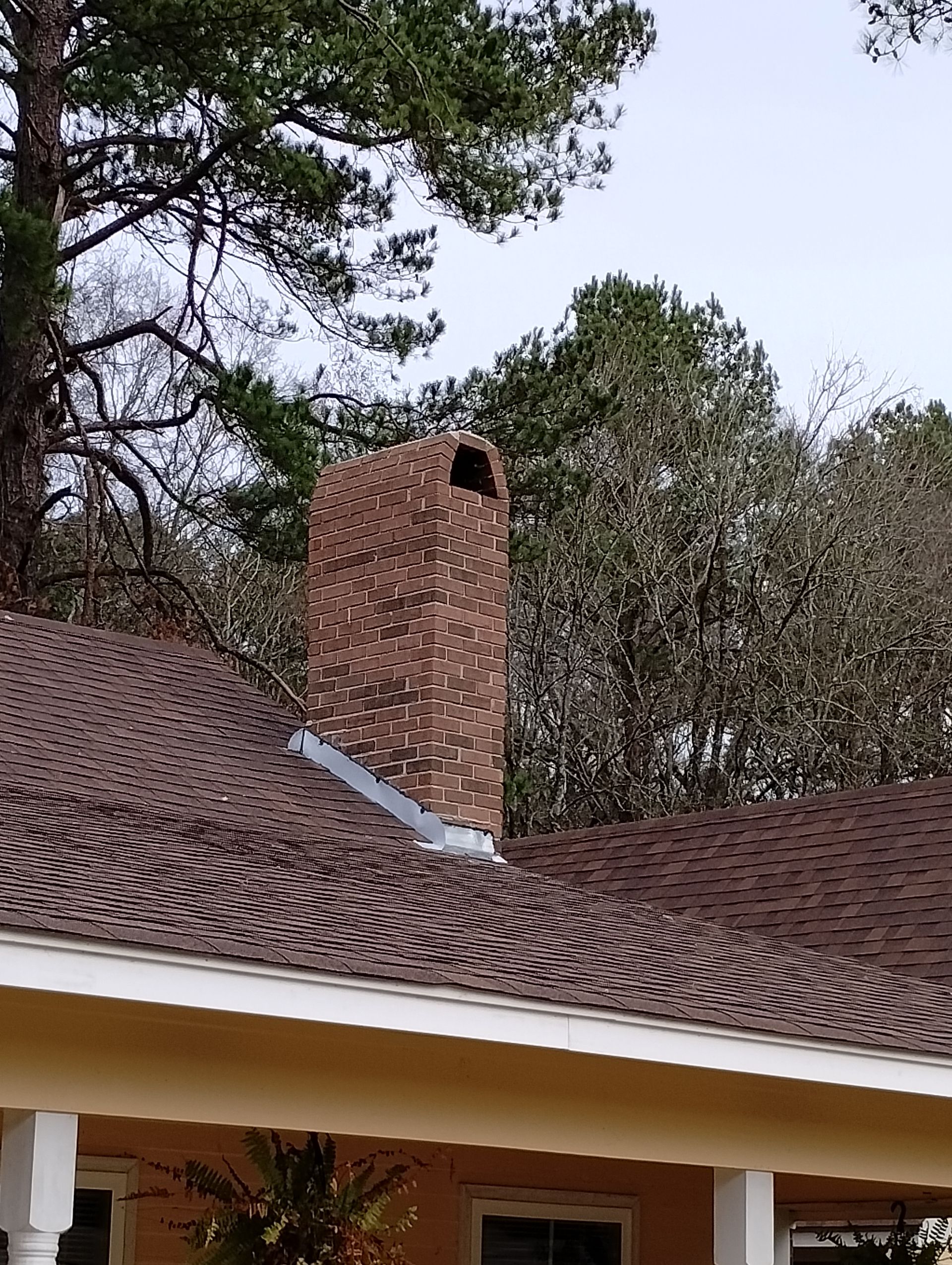 A chimney on the roof of a house with trees in the background