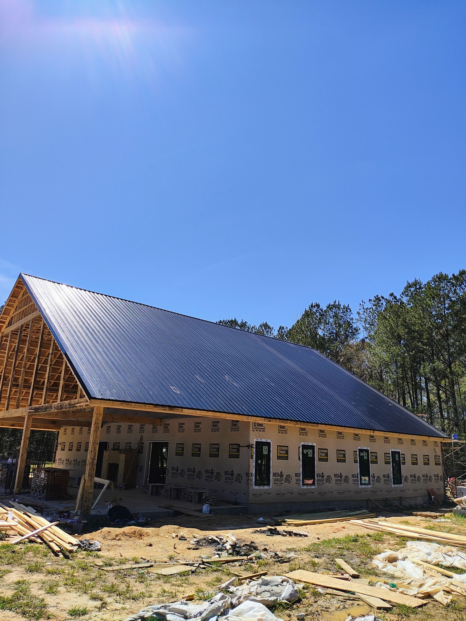 A house is being built with a black roof and a blue sky in the background.