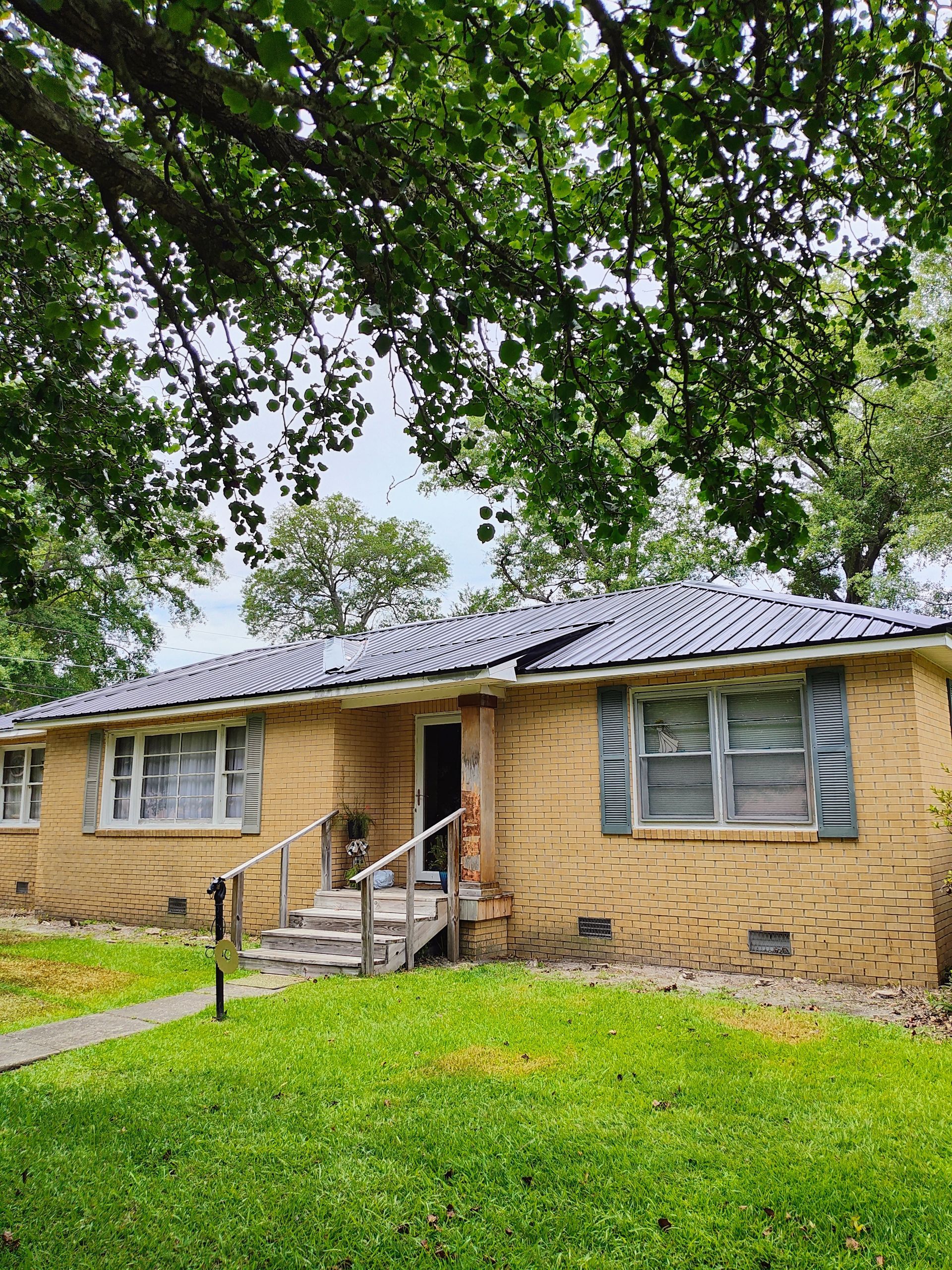 A brick house with a gray roof and a tree in front of it.