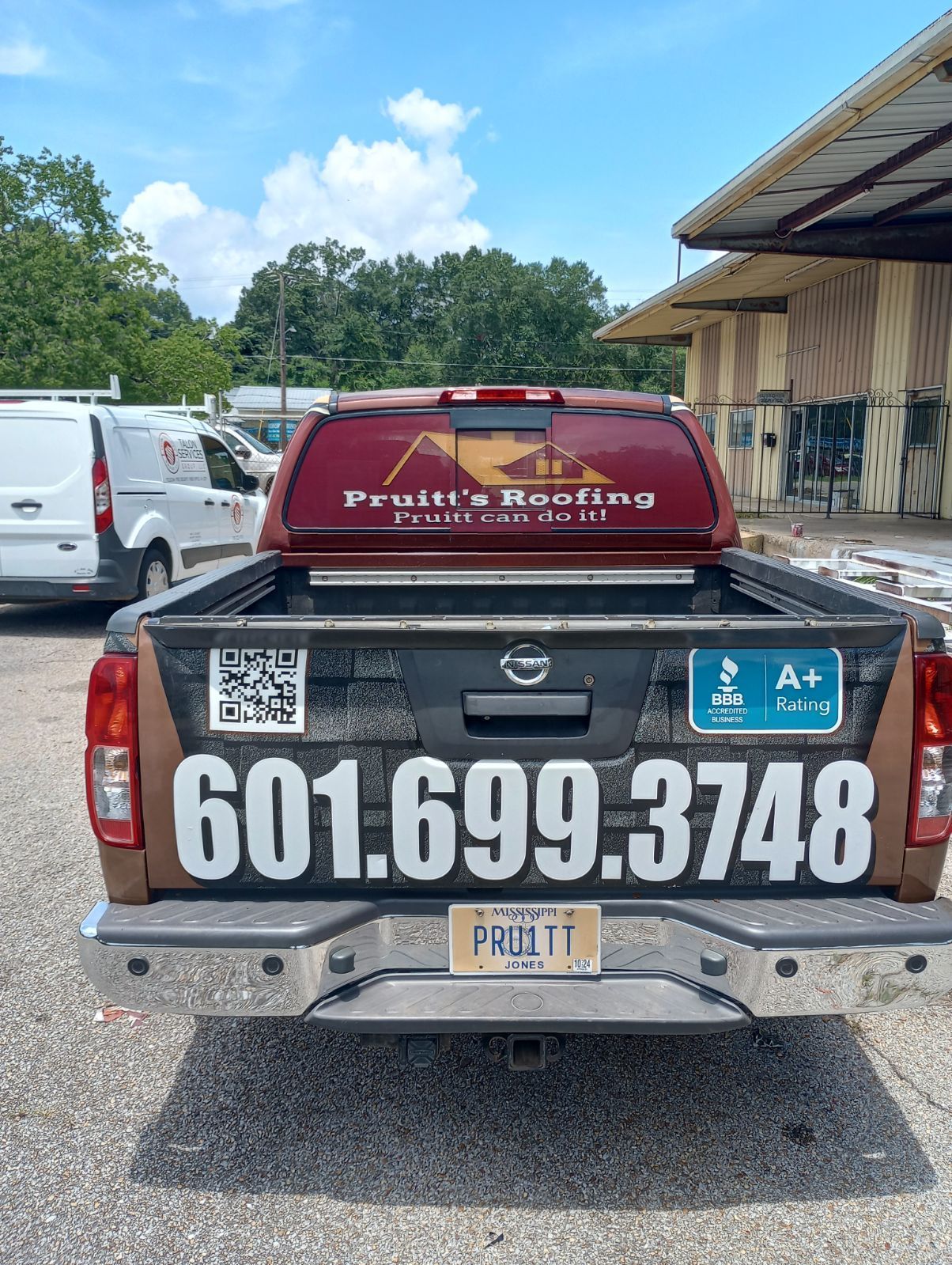The back of a truck with a phone number on it is parked in front of a building.