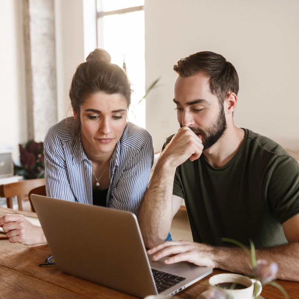 Woman and man looking at a laptop together at a wooden table, possibly discussing.