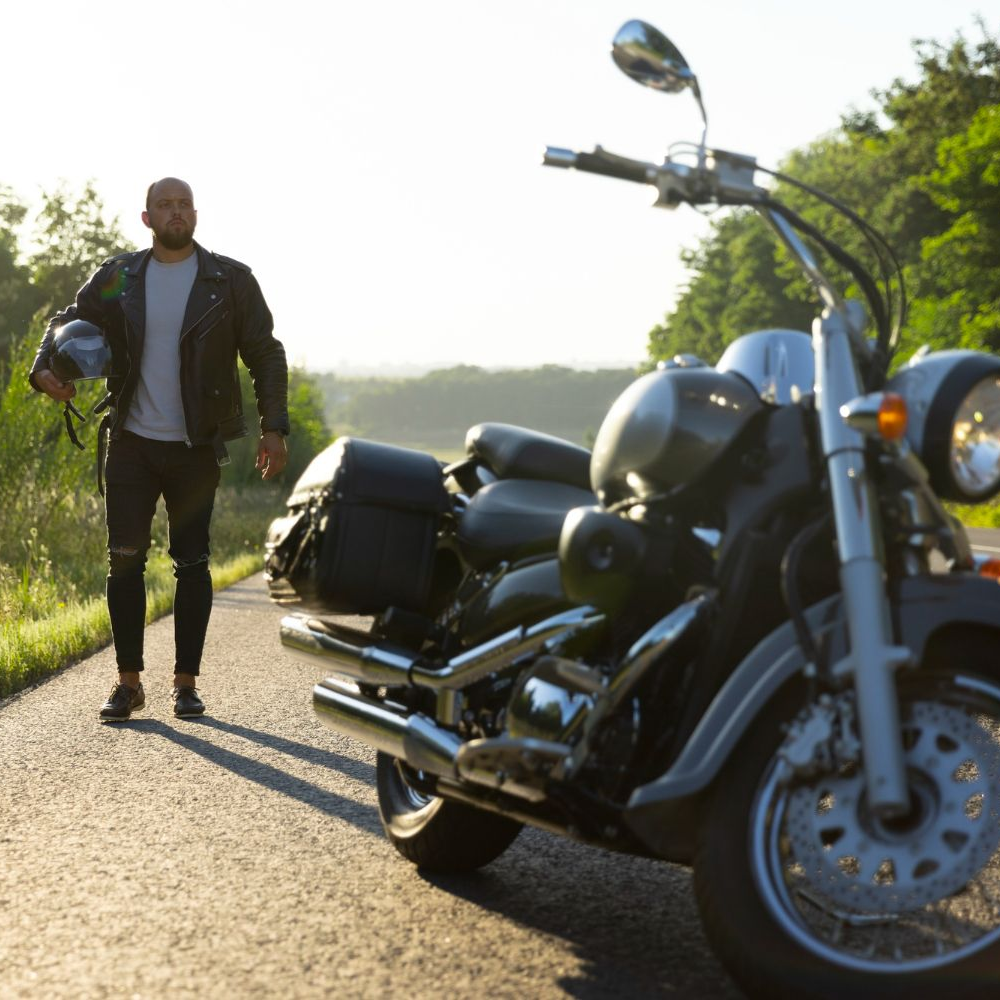 Man in leather jacket walks toward a motorcycle parked on a road.
