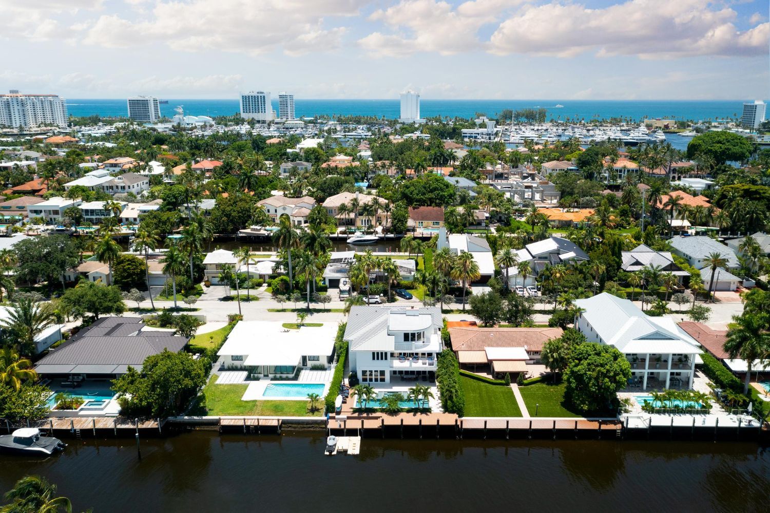 Aerial view of waterfront homes, trees, and buildings, with ocean visible in the distance.