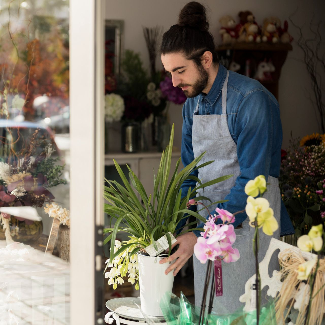 Florist in apron arranging flowers in a shop, seen through the window.