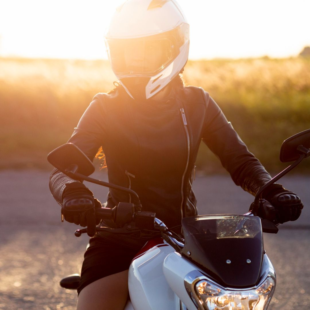 Person wearing a helmet and leather jacket rides a motorcycle at sunset.