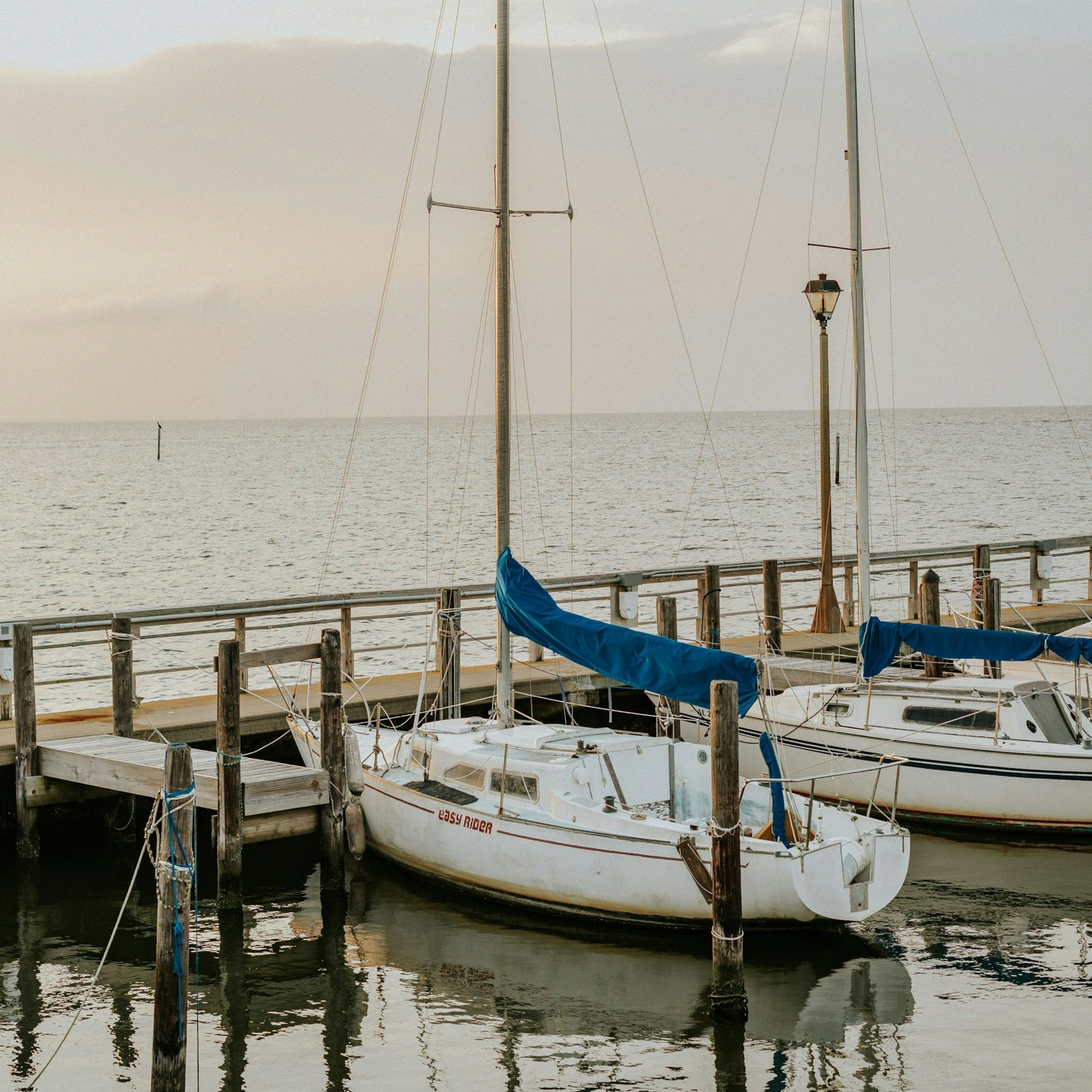 Sailboats docked at a pier on calm water; overcast sky.