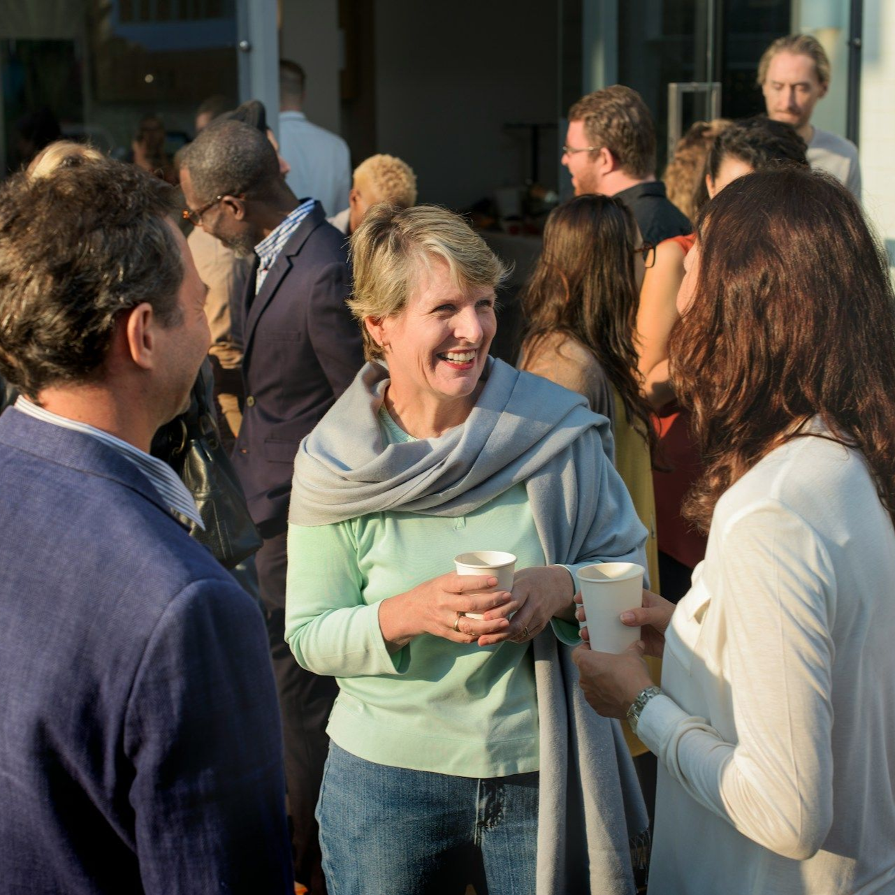Group of people socializing outdoors, holding cups, some smiling.