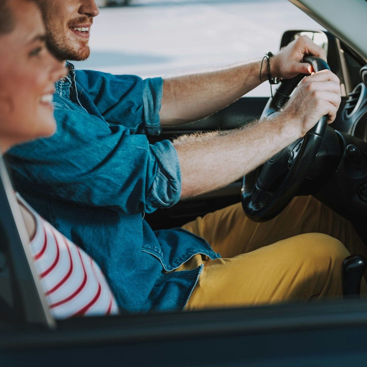 A person driving a car, smiling, with a passenger in the seat.