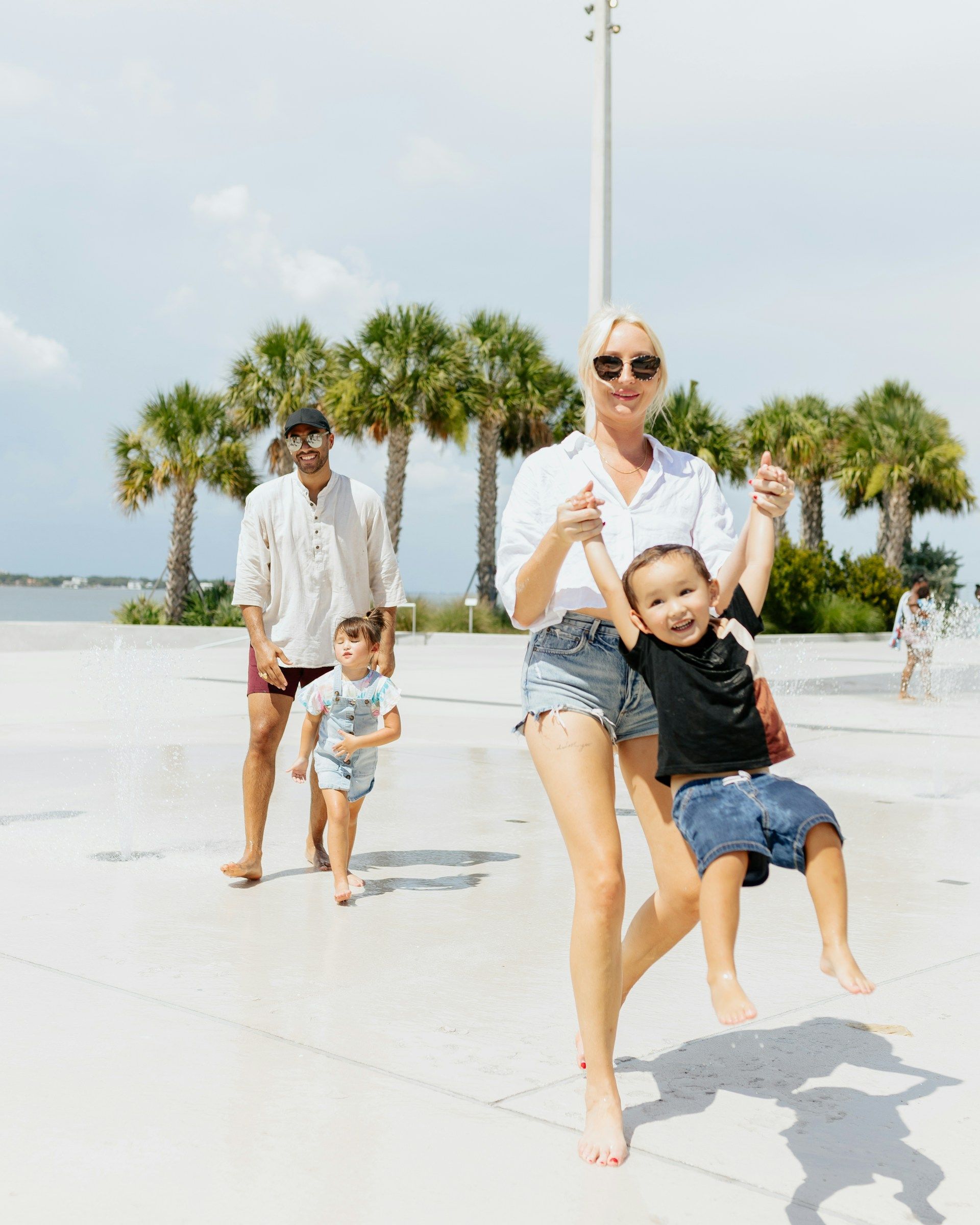 Family on a sunny day at a beach. A woman swings a child, another child runs, the man stands nearby.