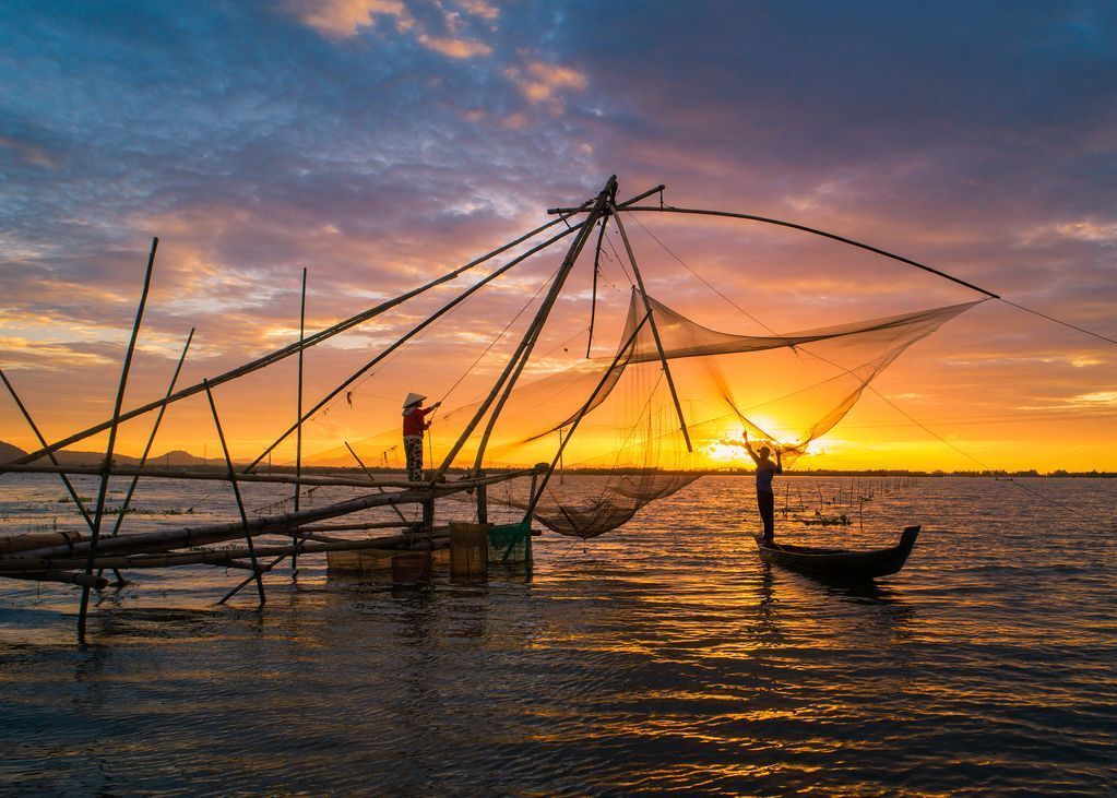 A man in a boat is fishing in the water at sunset.