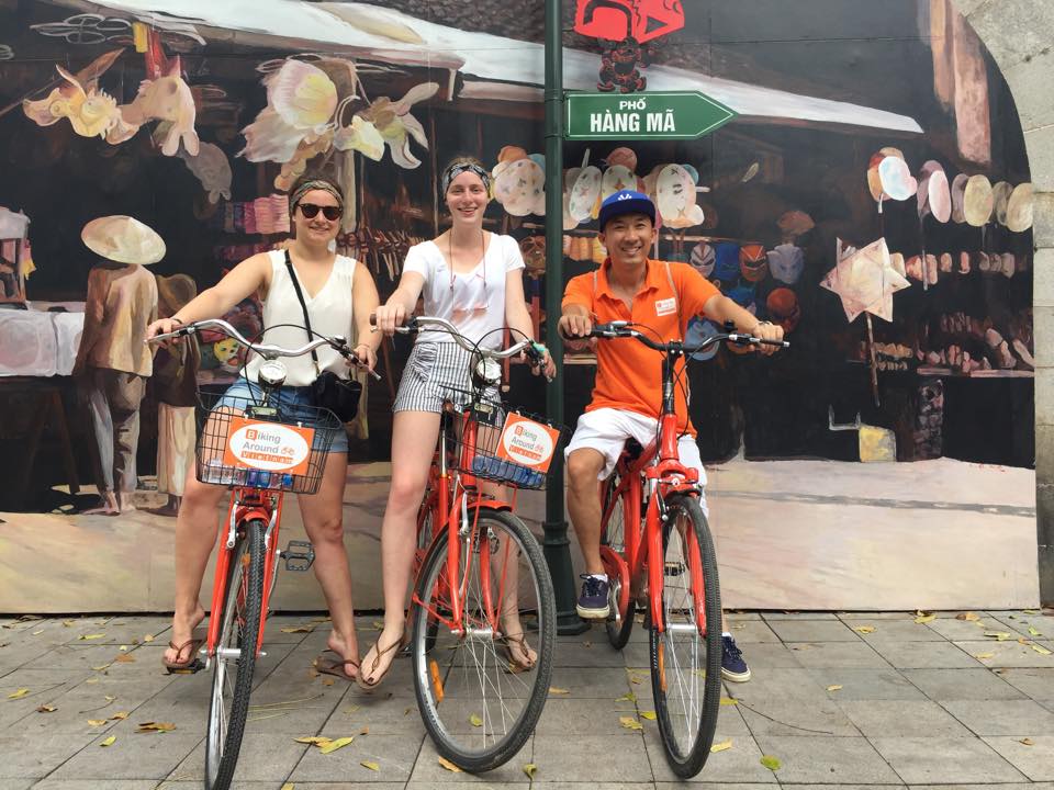 Three people are standing next to each other on bicycles.