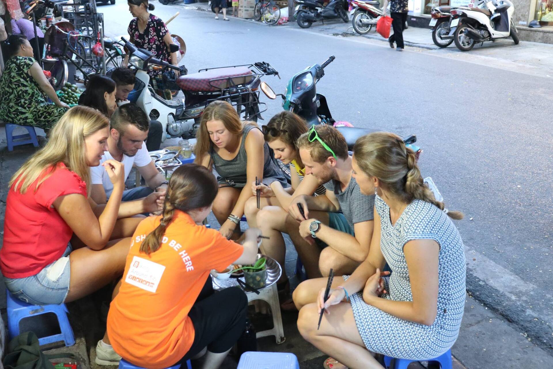 A group of people are sitting around a table on the side of the road.