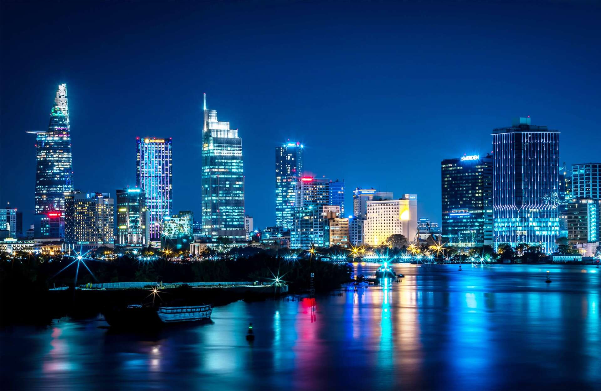 A city skyline at night with a river in the foreground.
