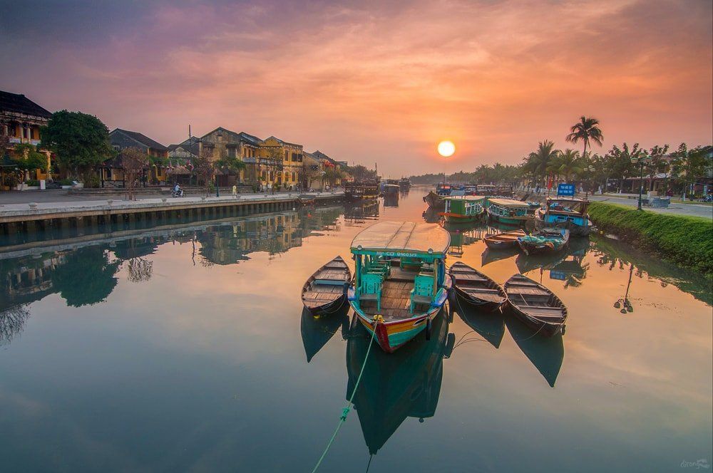 A group of boats are docked on a river at sunset.
