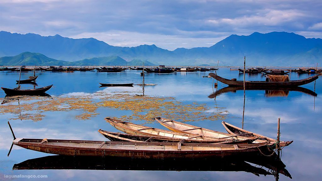 A group of boats are floating on top of a lake with mountains in the background.