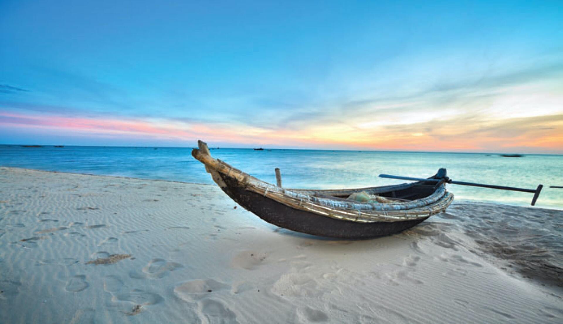 A boat is sitting on a sandy beach near the ocean.