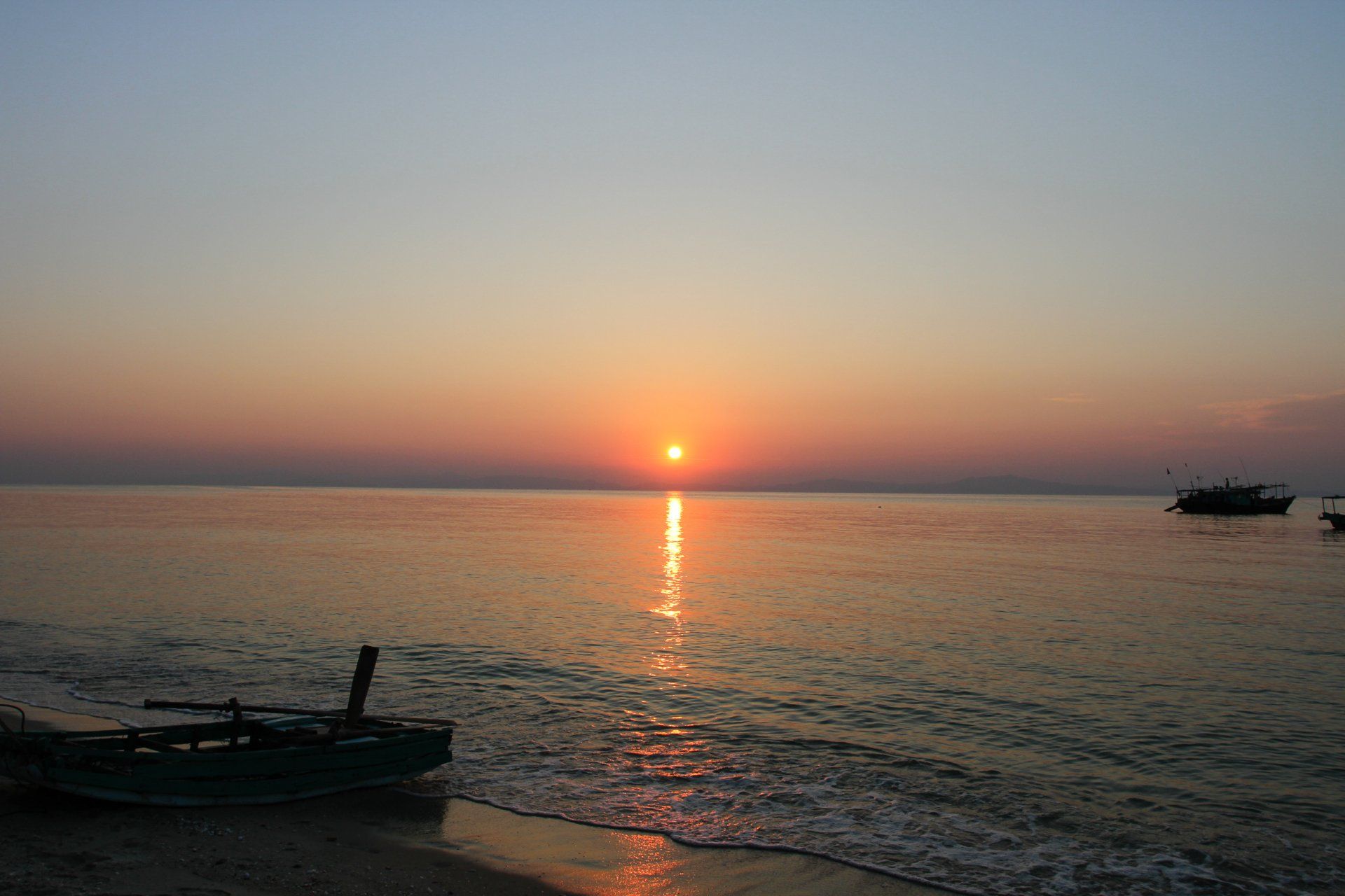 The sun is setting over the ocean with a boat in the foreground.