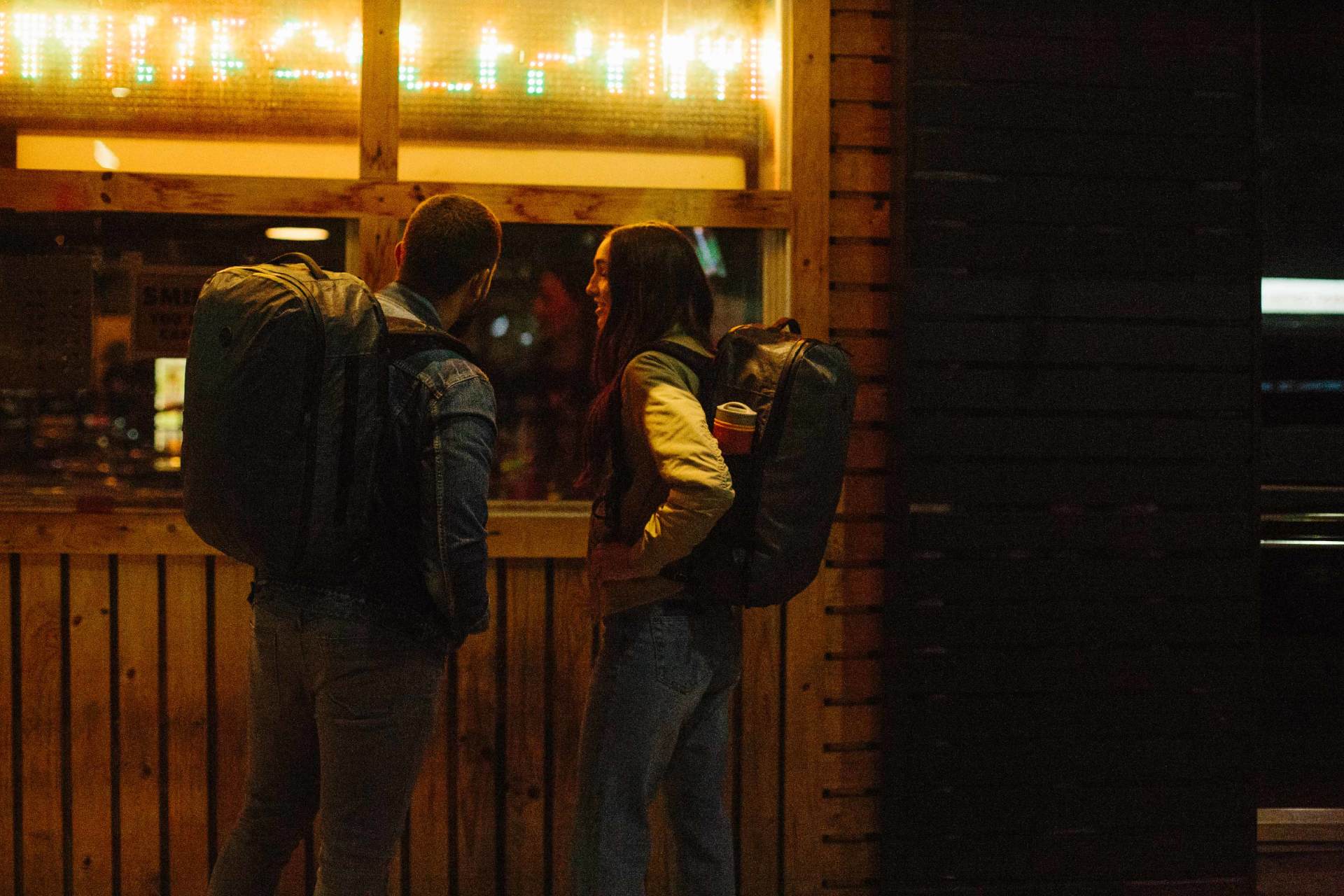 A man and a woman with backpacks are standing in front of a restaurant.