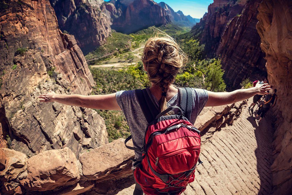 A woman with a backpack is standing on top of a mountain with her arms outstretched.
