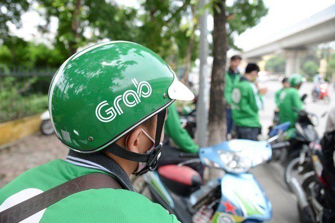 A man wearing a green grab helmet is riding a motorcycle.