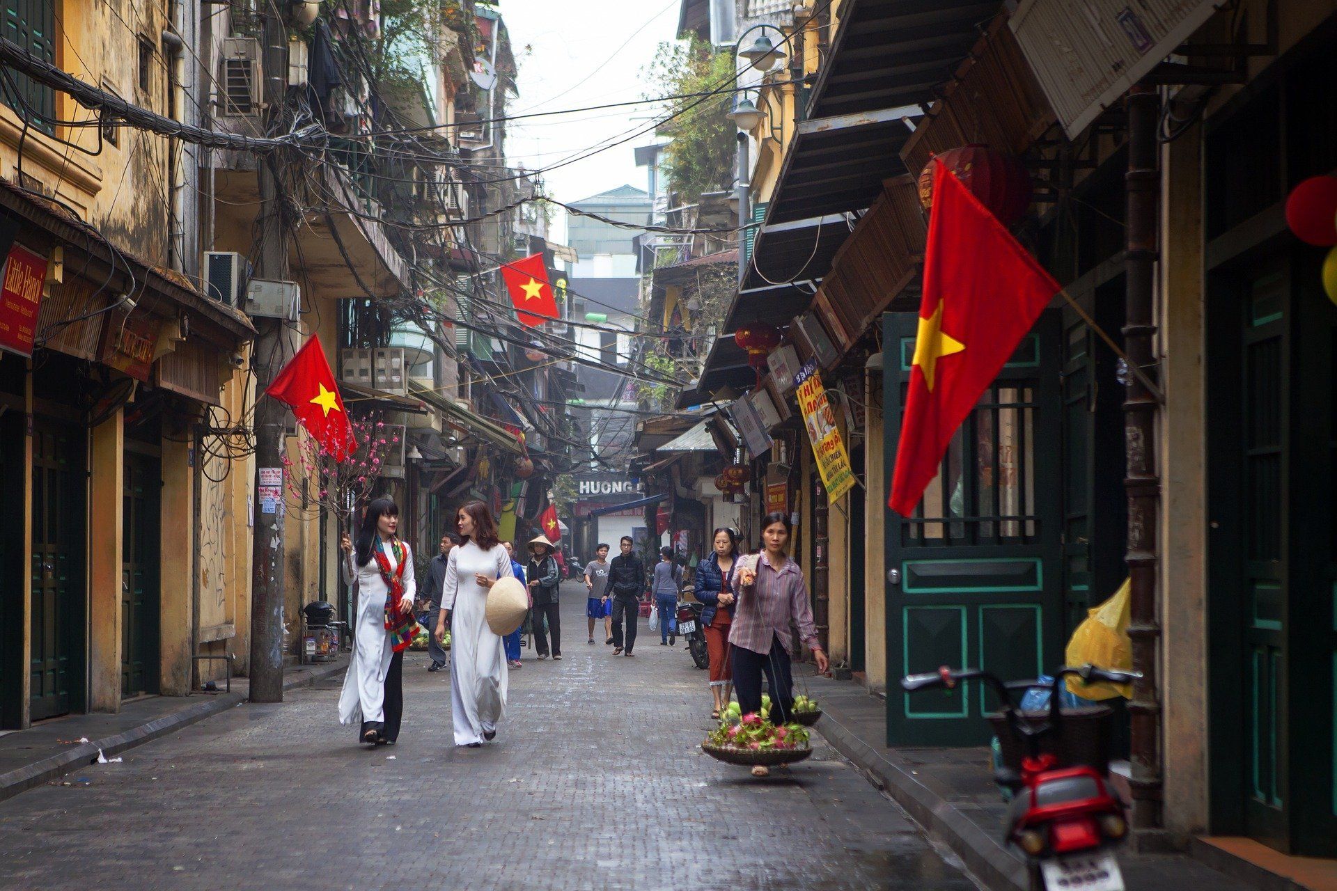 A group of people are walking down a narrow street with flags hanging from the buildings.