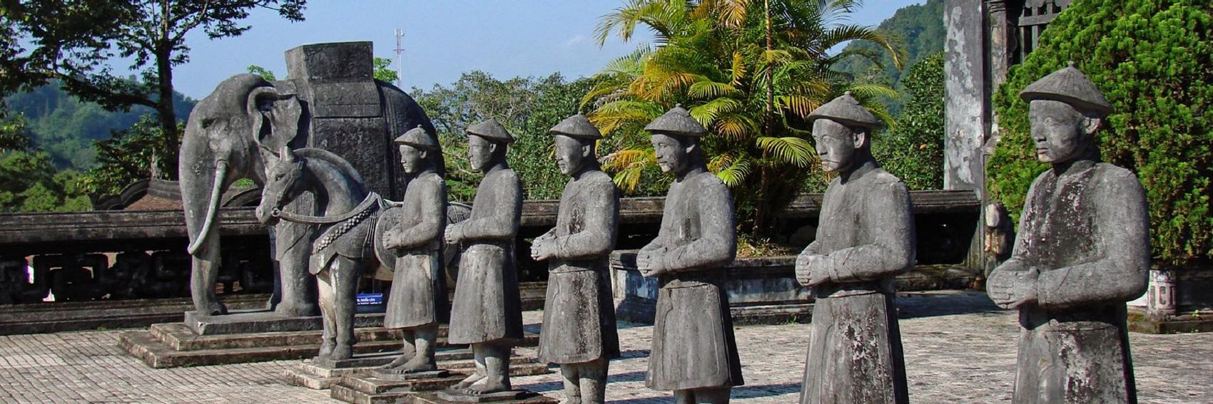 A group of statues standing next to each other in front of a statue of an elephant.