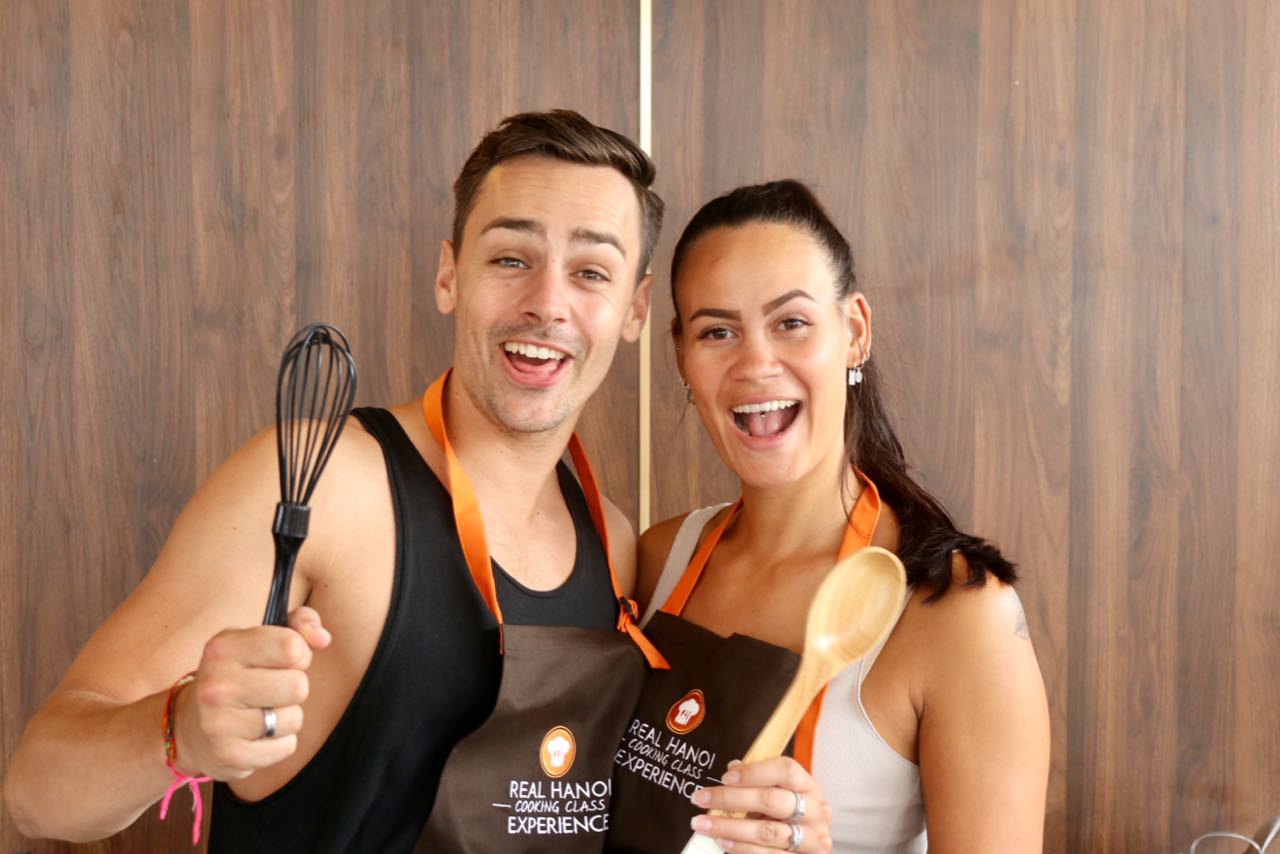 A man and a woman are standing next to each other holding spoons and whisks.