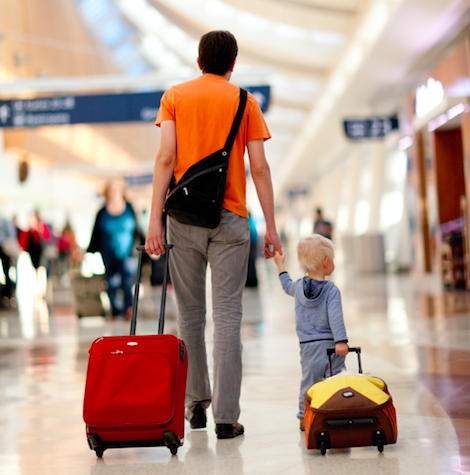 A man holding a child 's hand while pulling a suitcase