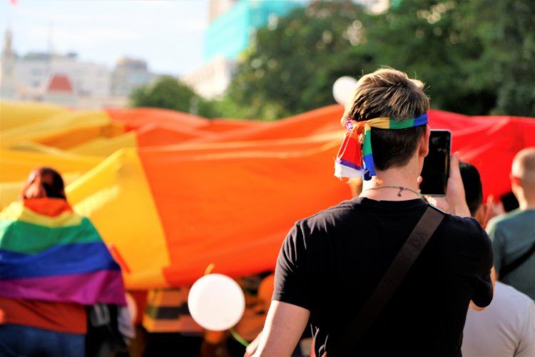A man is taking a picture of a group of people holding rainbow flags.