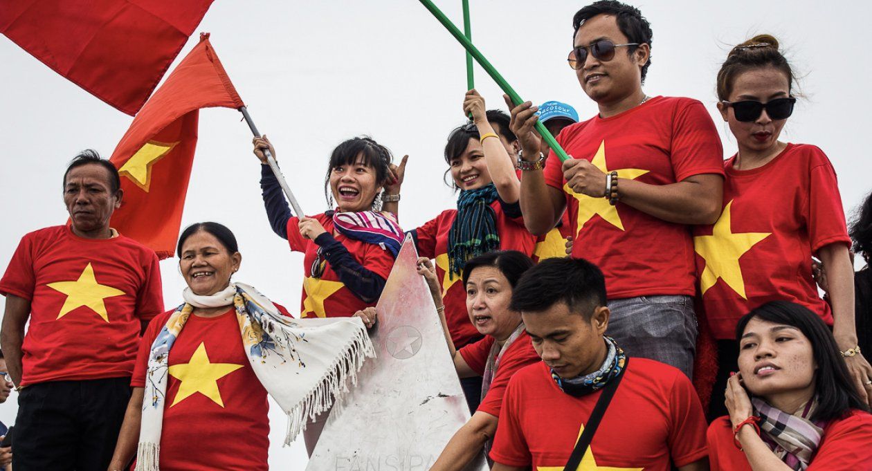 A group of people wearing red shirts with yellow stars are holding flags.
