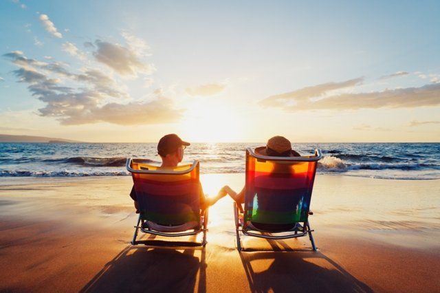 A man and a woman are sitting in beach chairs on the beach watching the sunset.