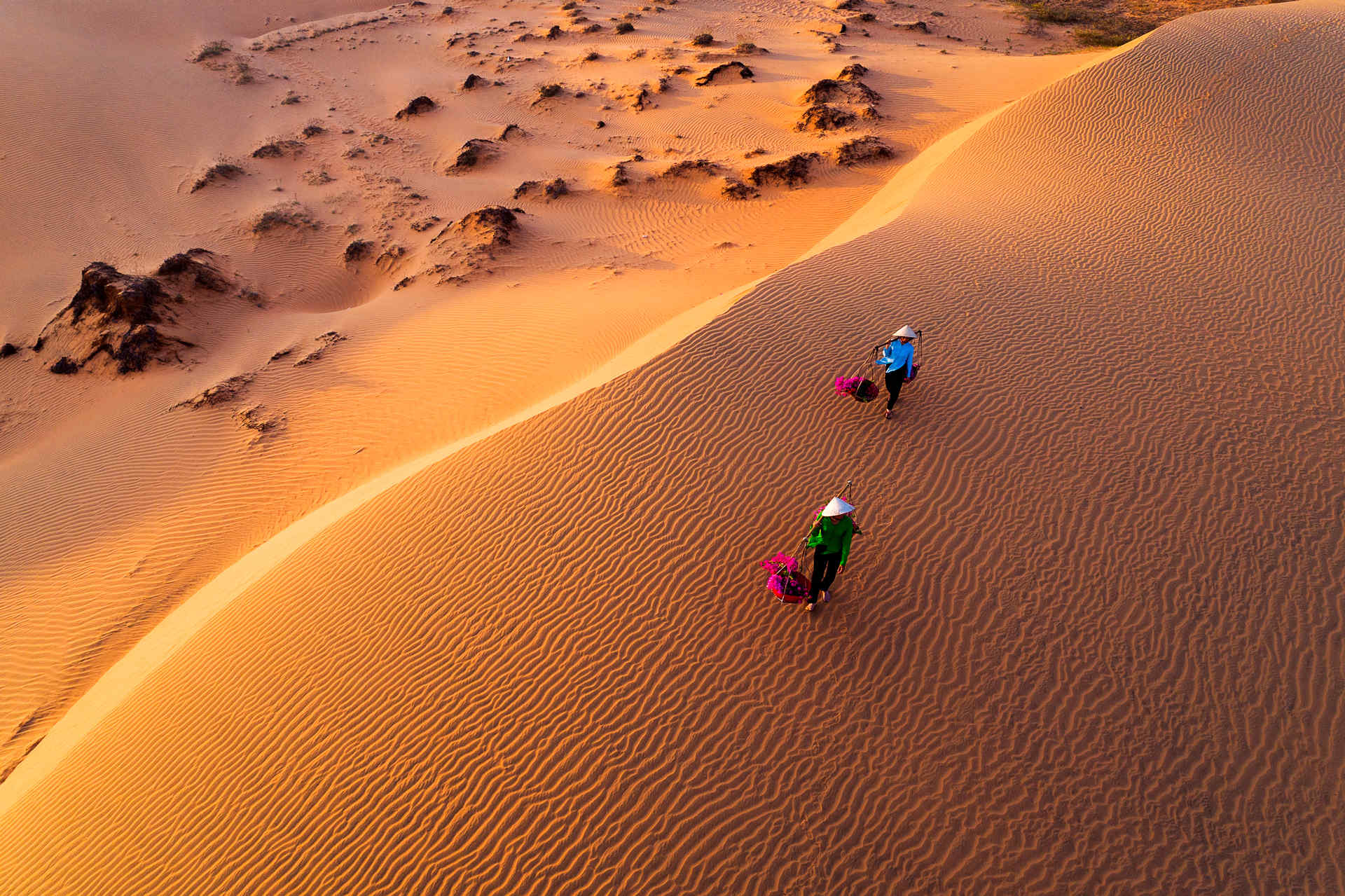 An aerial view of two people walking on top of a sand dune.
