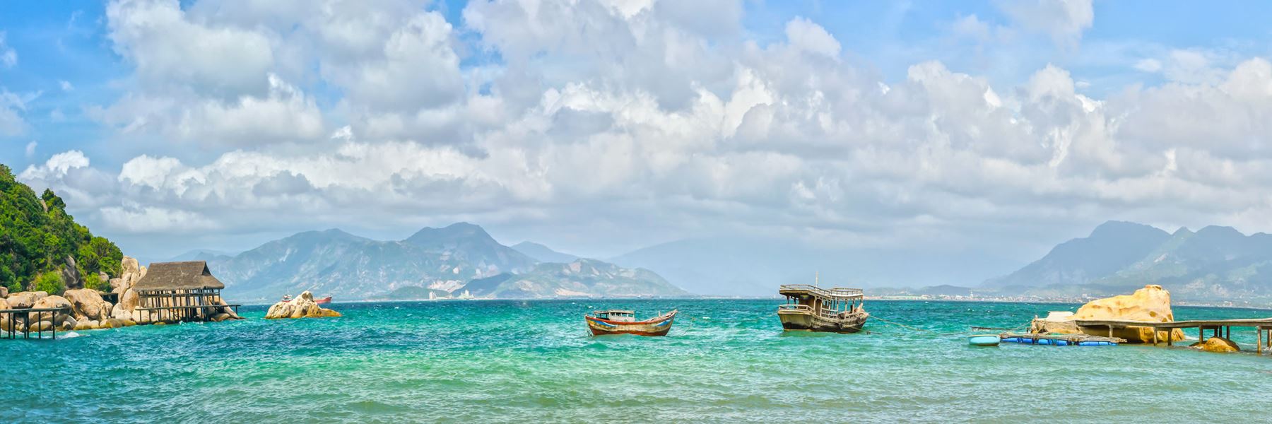 There are many boats in the ocean with mountains in the background.