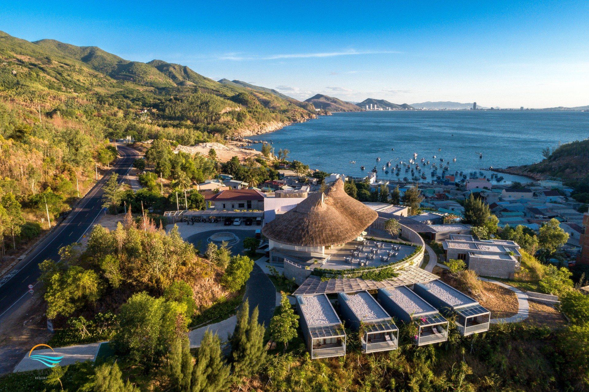 An aerial view of a resort surrounded by mountains and trees next to a body of water.