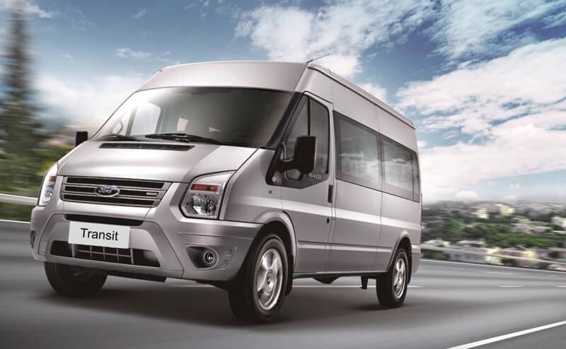 A silver ford transit van is driving down a highway.