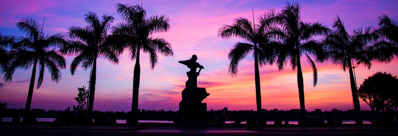 A sunset with palm trees and a statue in the foreground.