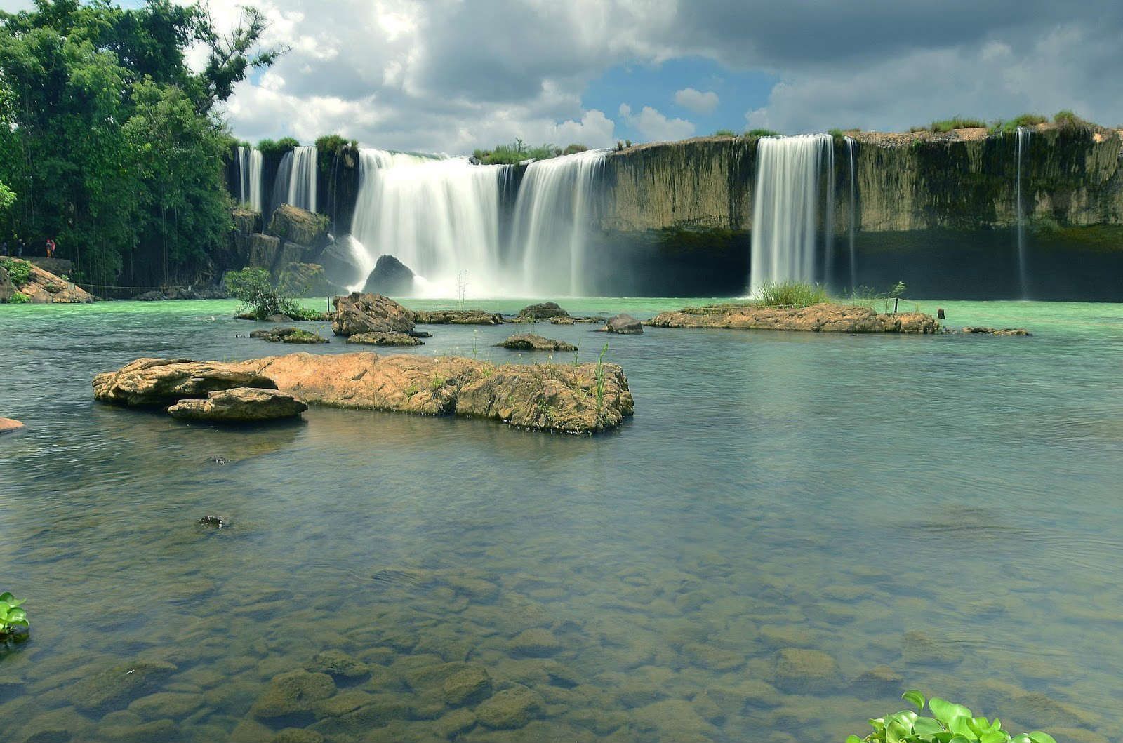 A waterfall is surrounded by trees and rocks in the middle of a river.