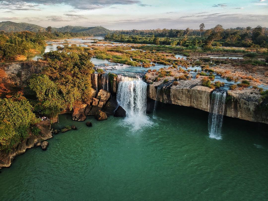 An aerial view of a waterfall in the middle of a river surrounded by trees.
